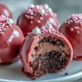 A hand dips an Oreo Truffle Ball into a bowl of melted pink candy coating.
