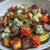 Golden caramelized edges highlight eggplant and peppers on a white platter topped with feta.