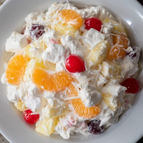 A refreshing bowl of Ambrosia Salad with bright fruits and creamy, sweet topping.