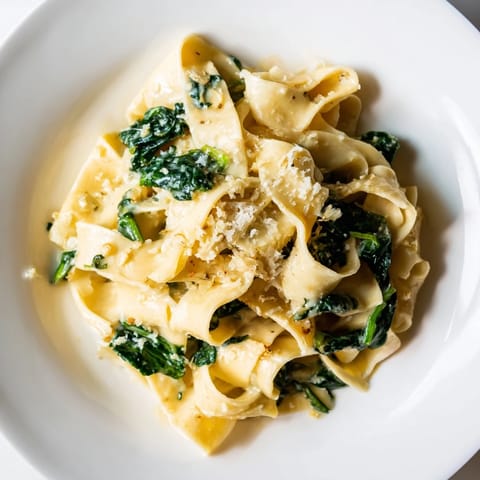 Freshly cooked egg noodles tossed with creamy spinach and garlic in a skillet, ready for a comforting dinner.