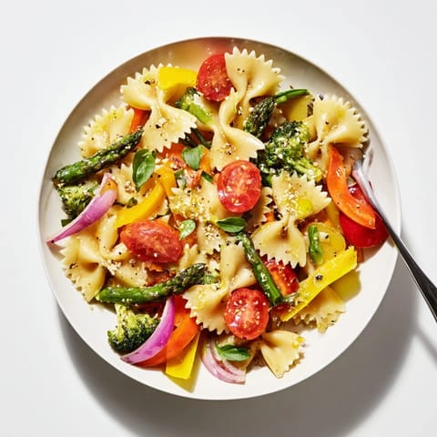 A serving of Rainbow Veggie Pasta Primavera on a rustic wooden table, featuring al dente farfalle with roasted veggies and a light lemon-garlic sauce.