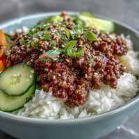 Easy Korean Beef Bowl with ground beef, fresh cucumber, carrots, and sesame seeds over fluffy white rice in a ceramic bowl.